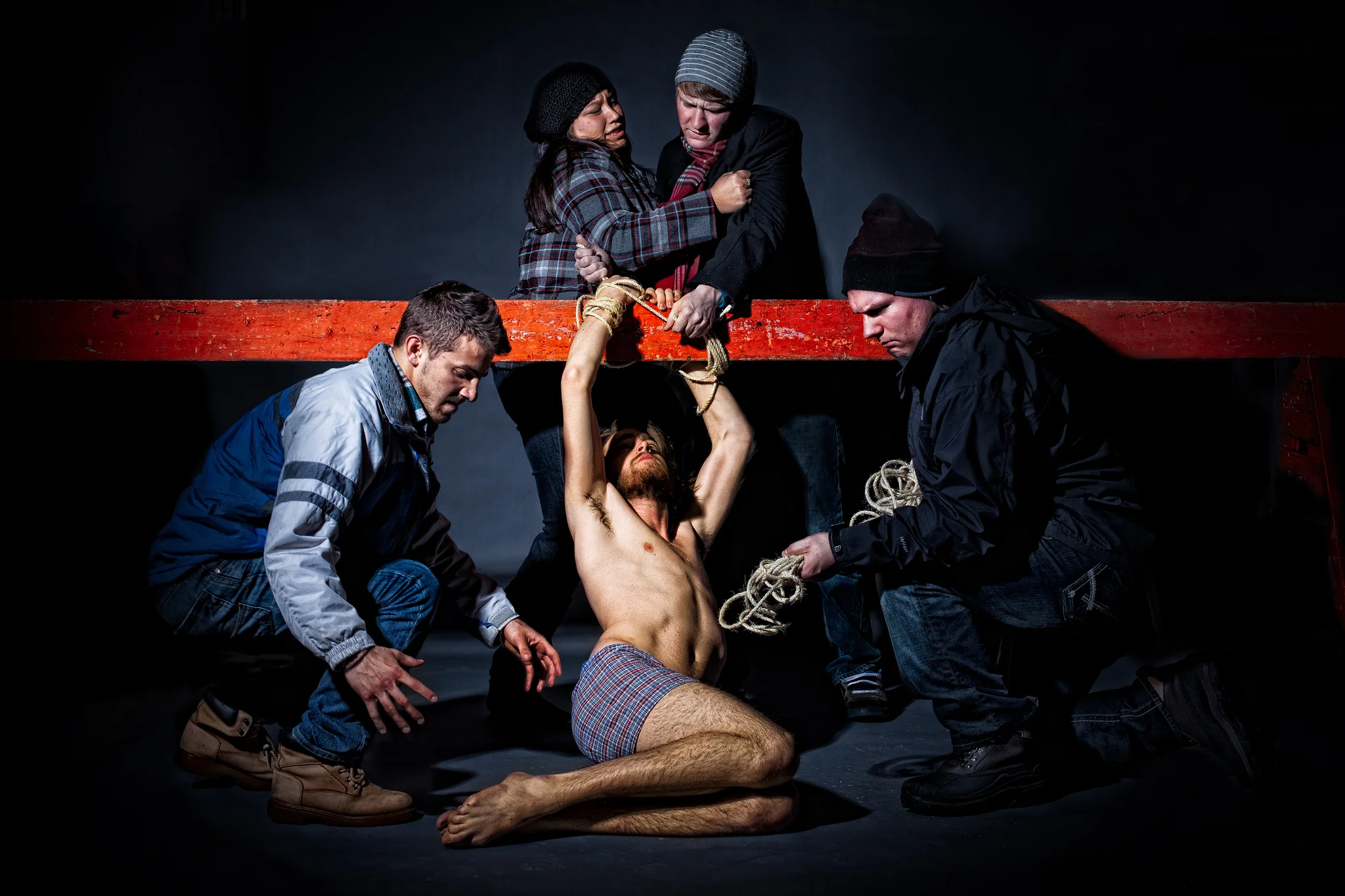 Winter-clad group restraining a seated bare-chested man